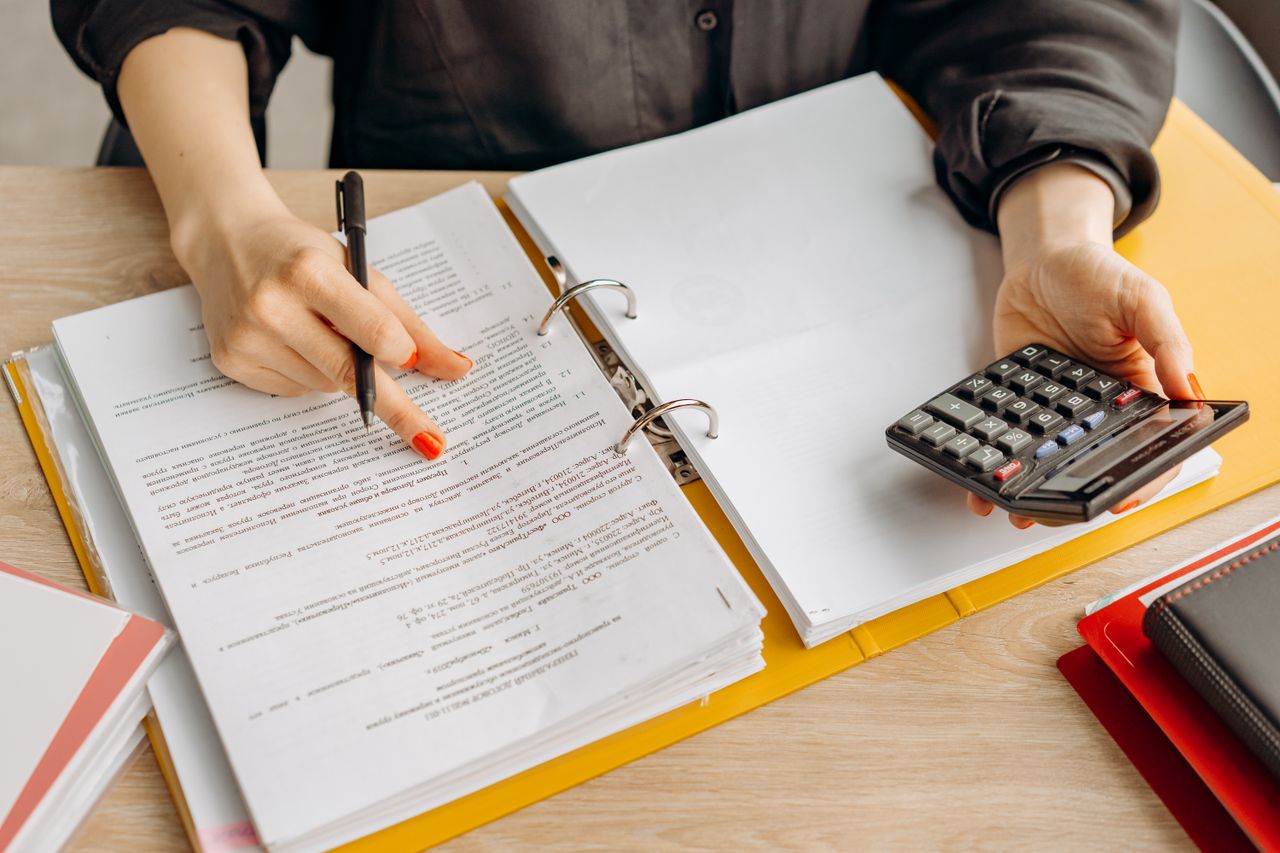 The Art of Drawing Readers In: Your attractive post title goes here A woman reviewing documents and using a calculator on a wooden table.